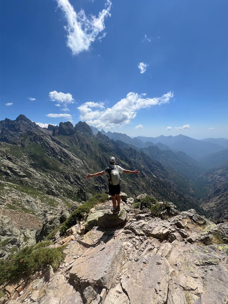 Homme au sommet d’une montagne, bras ouverts face au paysage, représentant la liberté et la réussite d’un challenge